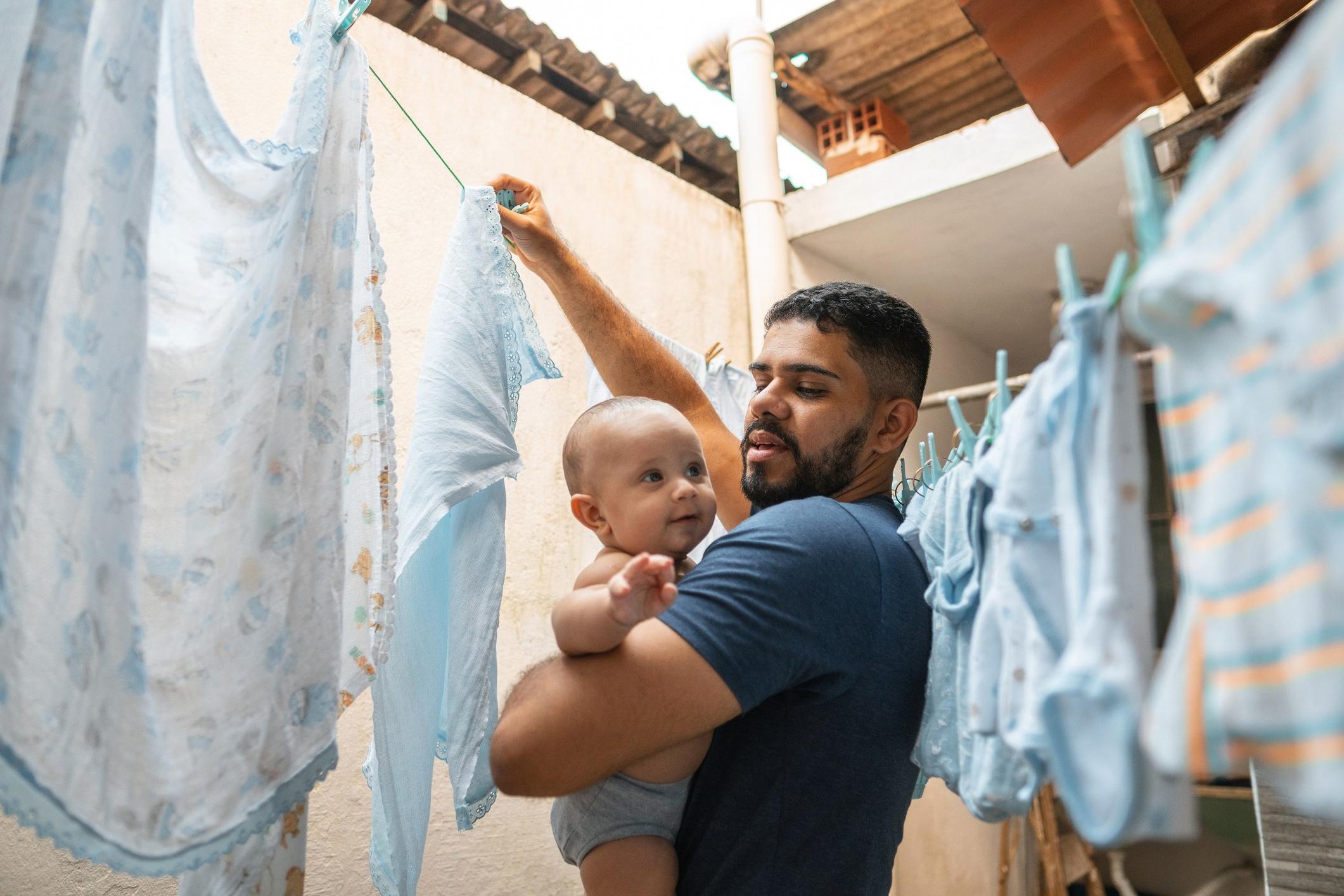 Father line drying clothes while holding a baby