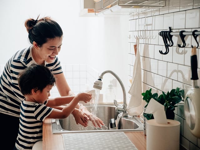 Asian baby boy learn to washing dish with his mother in kitchen.