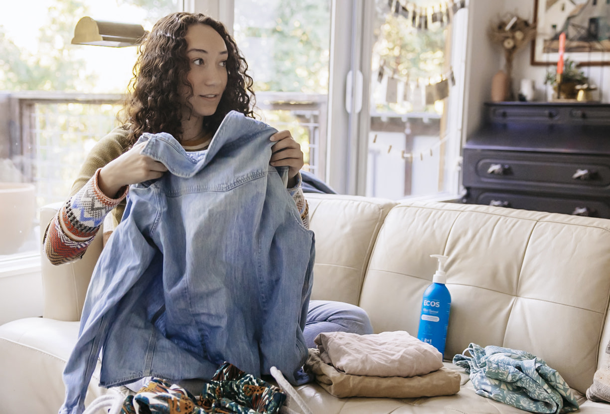 Woman folding laundry on a couch with a ECOS bottle next to her on the couch