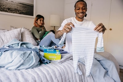 Dad holding up onesie with mom and baby in background with ECOS laundry sheets