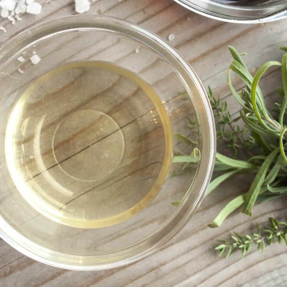 A small glass bowl of vinegar with a rosemary sprig
